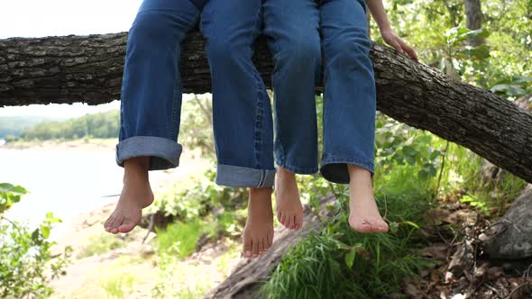 Two girls swing their feet on a big branch