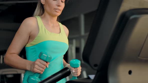 Caucasian Woman on a Treadmill Walking and with Two Dumbbells