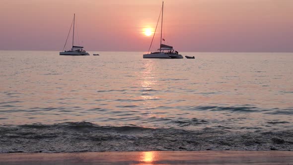 Sailboats in front of pastel colored sunset at beach - ultra slow motion tilting up