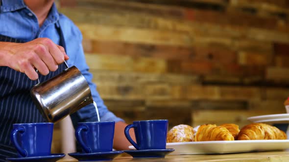 Waiter pouring milk in coffee at counter