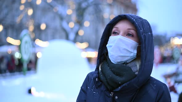 A Young Woman in a Medical Mask Stands Against of a Festively Decorated City