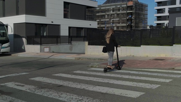 Unrecognizable woman crossing the street on electric scooter