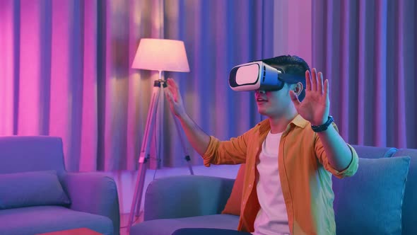 Asian Man Wearing Vr Headset At Living Room, Using Hand Touching And Slide, Cyan And Magenta Colors
