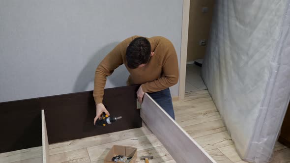 Young Man in Brown Sweater Assembles the Bed with a Screwdriver