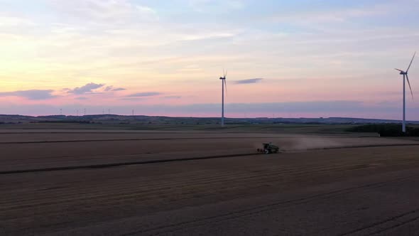 Drone rotating around a harvesting combine surrounded by wind turbines.