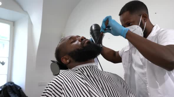 Barber blow-drying and brushing beard of customer