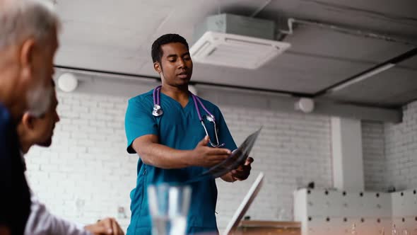 Young African Medical Man Doctor Making Report To Colleagues on Results of Patient Chest X-ray Image