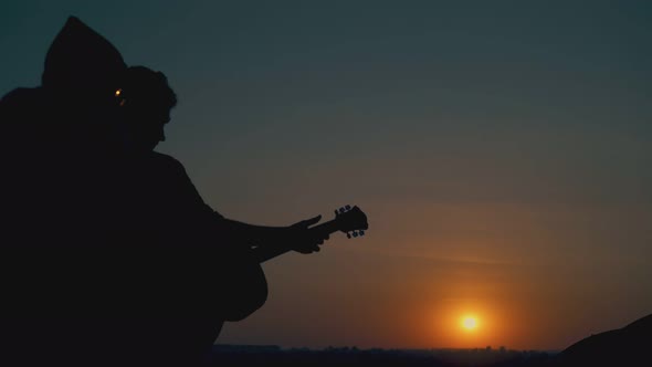 Silhouettes of Man Playing Guitar and People Resting at Camp
