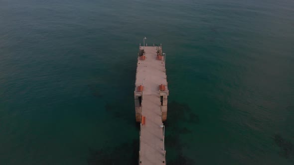 Backward flight above green calm ocean sea waters and old Porto Santo island beach pier in Portugues