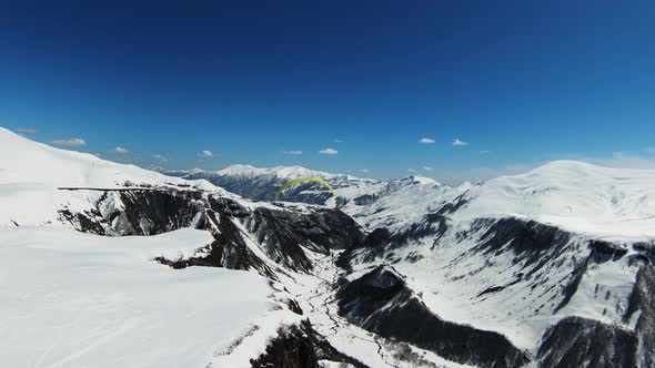 Paraglider coming down against the background of the beautiful river and the snow-covered hills