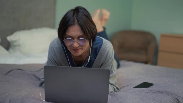 Positive mature woman waving hand at laptop