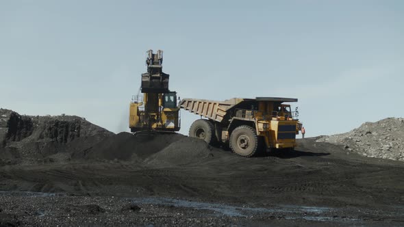 Excavator Boom with Bucket Filled with Coal Turns and Spills Into Back of Truck