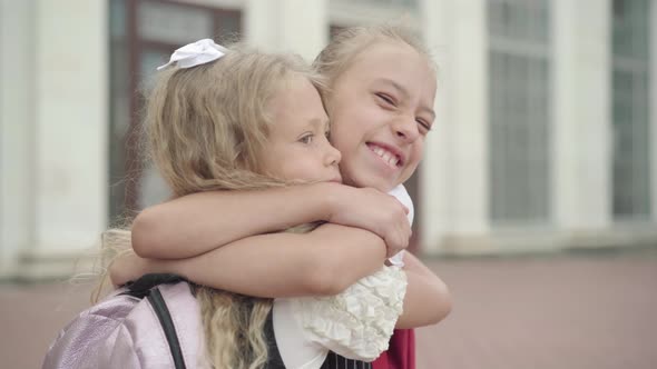 Close-up of Happy Children Hugging Outdoors. Portrait of Caucasian Schoolgirls Meeting at School