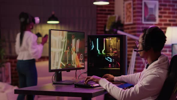 African American Man Having Fun Playing Intense First Person Shooter While Girlfriend is Relaxing in