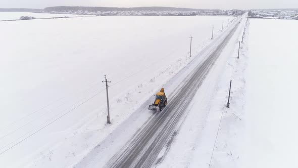 Aerial view of Yellow tractor with bucket rides on the Snow Covered Country Road 19