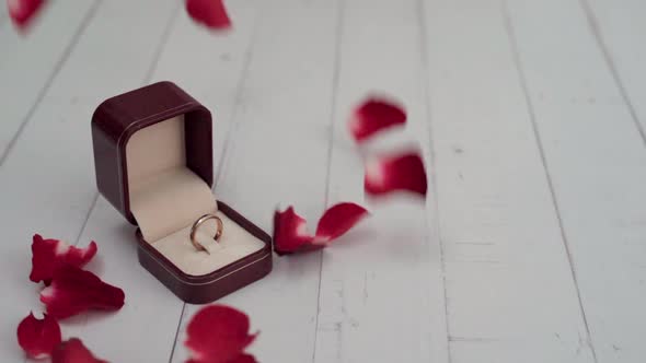 Ring in the box set on white wood table and rose petals falling