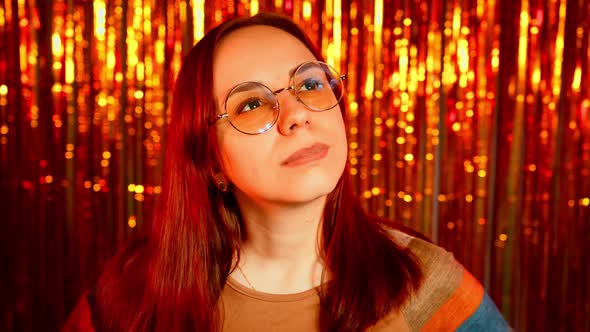 Thoughtful Pretty Woman in Glasses on Background of Shiny Tinsel