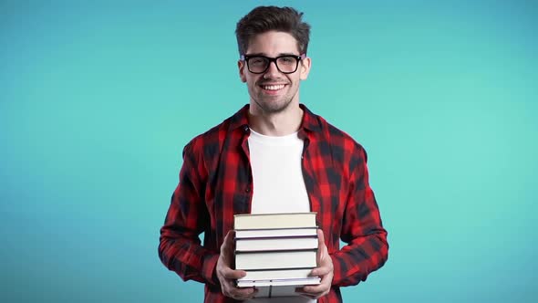 European Student in Red Plaid Shirt on Blue Background in Studio Holds Stack of University Books