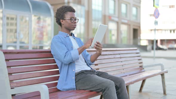 Young African Man Using Tablet While Sitting Outdoor on Bench