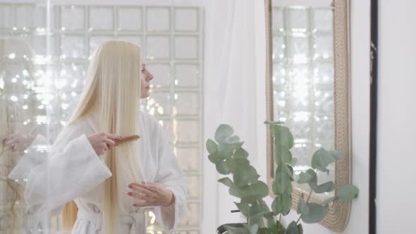 Portrait of Attractive Young Blond Woman Wearing Bathrobe With Natural Makeup Looking in Mirror