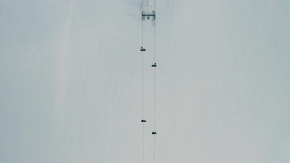 Aerial view of people going up a snow capped mountain with a chairlift, going down skiing and doing