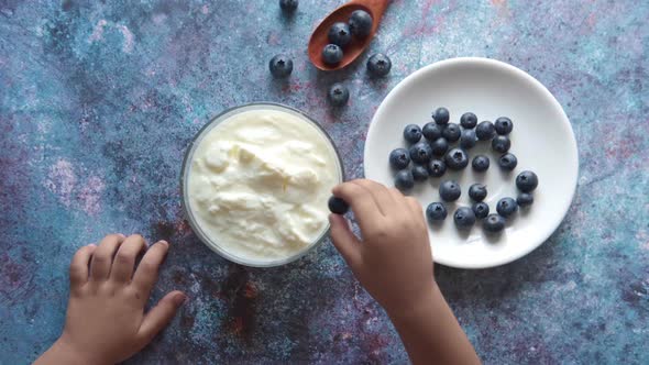Child Hand Putting Blue Berry on Fresh Yogurt