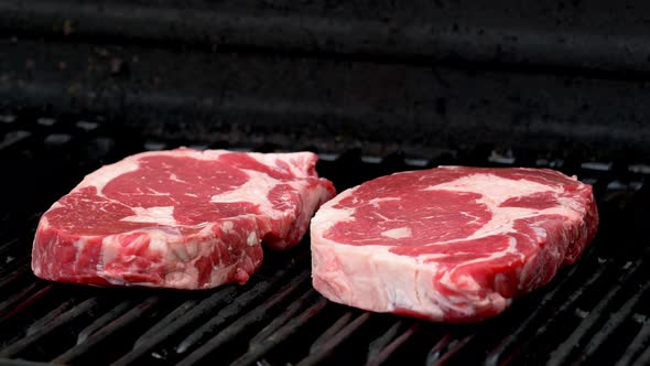 Two raw rib-eye steaks getting ready to cook on a grill.