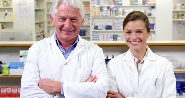 Smiling pharmacists standing with arms crossed in pharmacy