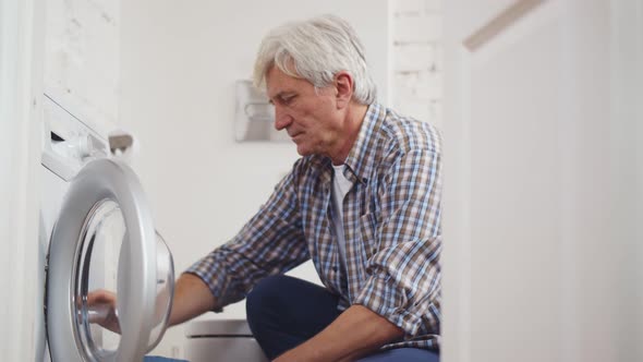 Senior Man Loading Clothes Into Washing Machine in Bathroom