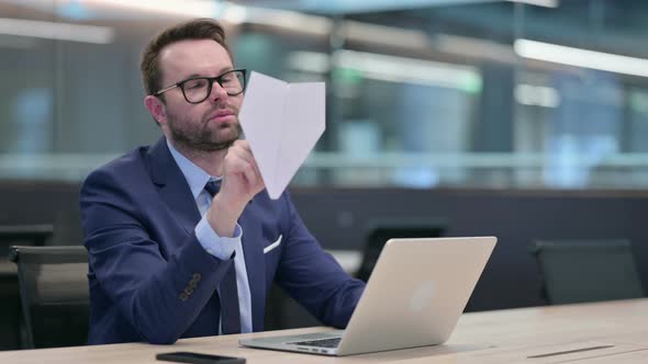 Middle Aged Businessman Holding Paper Plane in Office