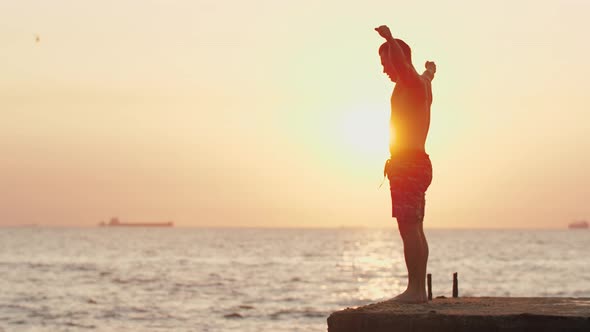 Young Man Jumping From Sea Pier and Doing Frontflip During Beautiful Sunrise Slow Motion