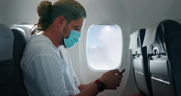 Caucasian Man in Medical Mask Reads on His Phone