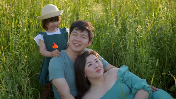 Korean Family with Their Daughter Lie in a Field in the Grass at Sunset