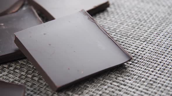 Dark bitter chocolate broken into pieces with crumbs close-up on a textured plastic mat