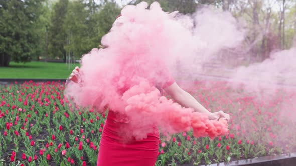 A Girl with Makeup with Rainbow Braids in Red Dress Posing in Red Smoke Against the Background of a