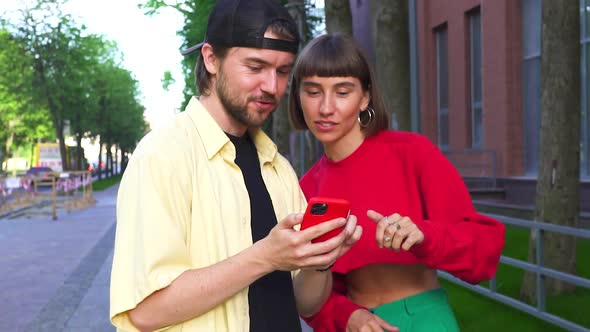 Millenial Couple on Urban Street Using Phone and Discussing with Happiness