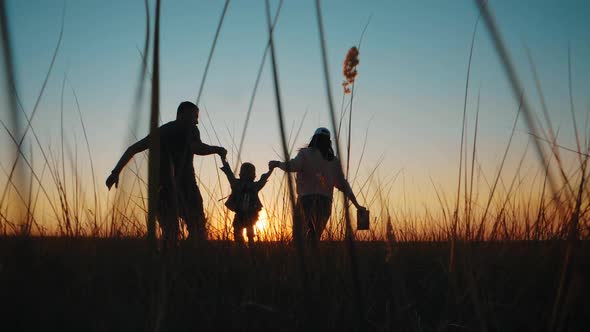 Happy Young Family Together with Their Little Child at Sunset. People Silhouettes on Summer Sunset