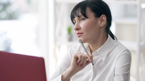 Thoughtful Concentrated Businesswoman Sitting in Office with Laptop Looking Away