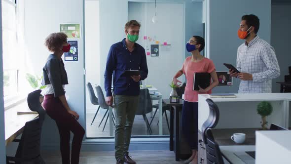 Portrait of diverse colleagues wearing face masks discussing together at modern office