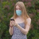 A young girl in a protective medical mask looks at the phone and sends messages - VideoHive Item for Sale