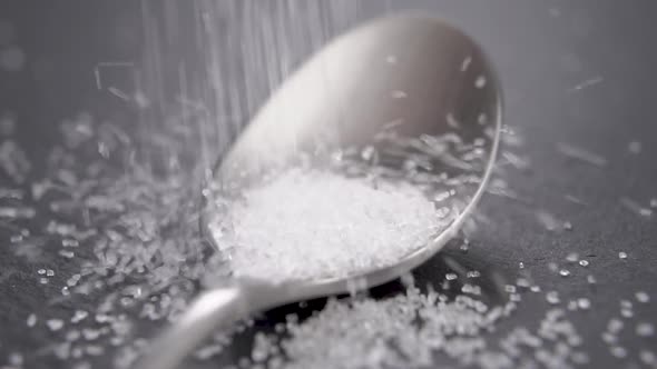 Sugar pouring in a teaspoon on a dark kitchen slate surface