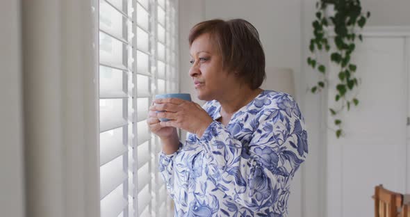 Happy african american senior woman enjoying drinking cup of tea looking out of window