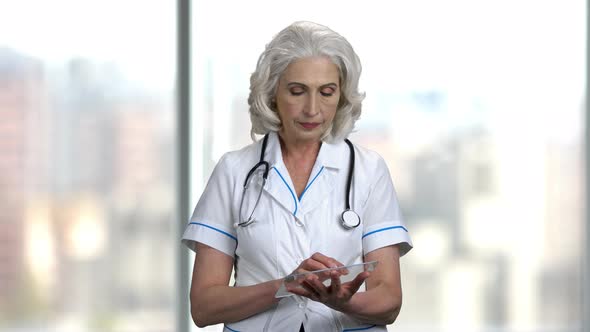 Mature Doctor Using Glass Tablet on Blurred Background.