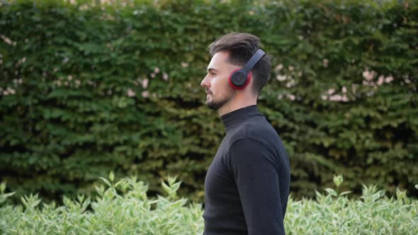 Side View Smiling Confident Young Man in Headphones Walking in Spring Summer Park