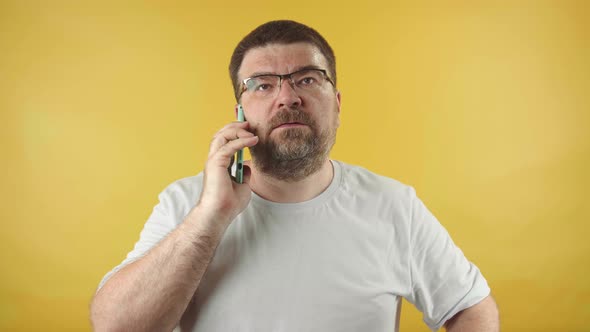 European caucasian man with a beard and glasses is happily talking on a smartphone