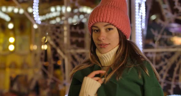 Portrait of Cute Caucasian Girl in Winter Clothes Standing in Front of Colorful Carousels and