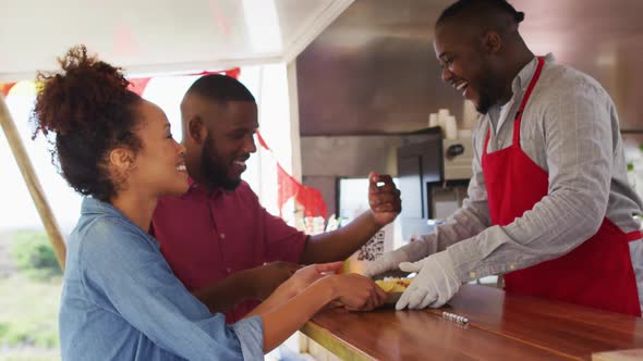 Smiling african american male food truck owner serving food to happy diverse couple
