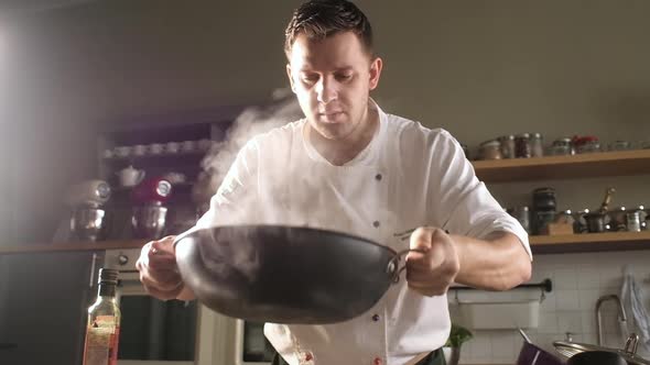 chef in modern kitchen mixes ingredients in wok. man throws pasta in the pan.