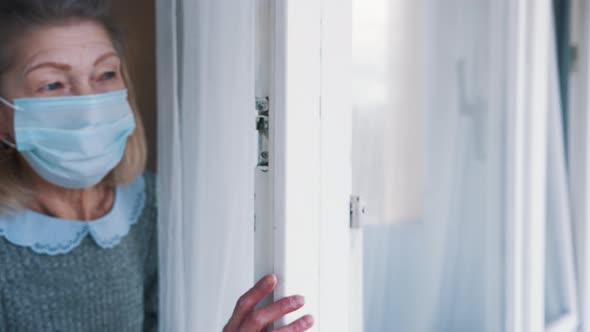 Elderly Gray Haired Woman with Medical Mask Looking Through the Window