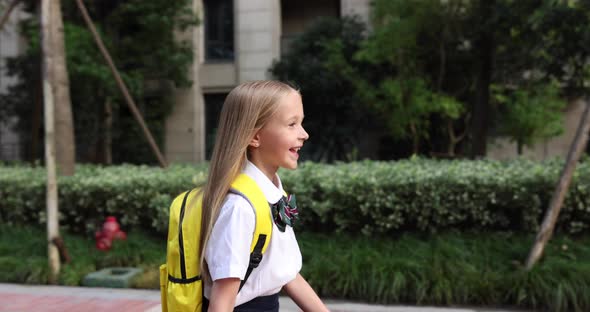 Happy Little Caucasian Blonde Girl Seven Years Old in Uniform with Yellow Backpack Going Back to